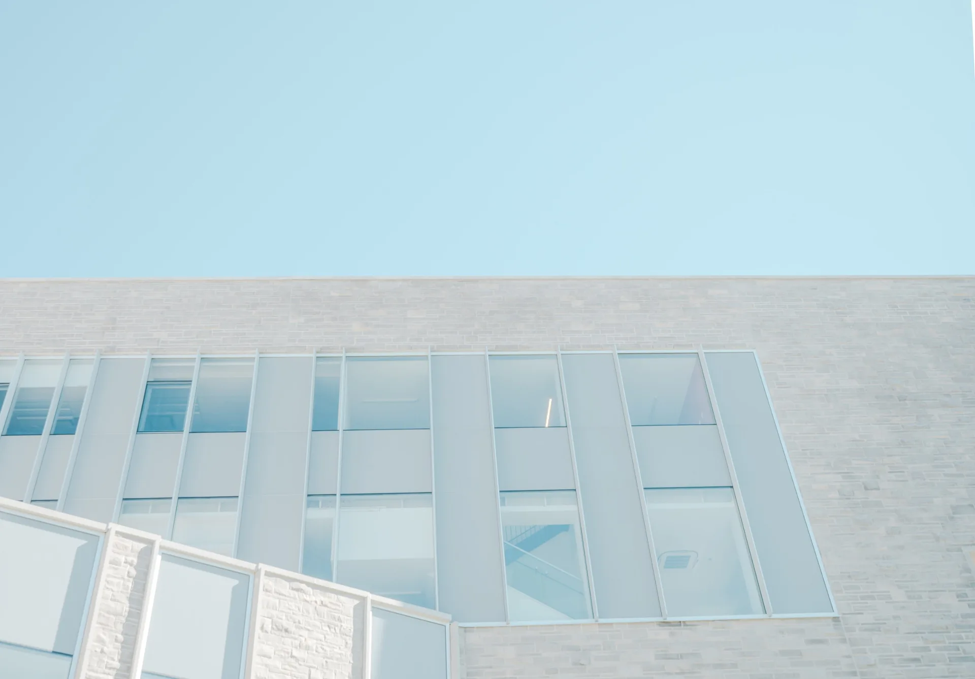 Helle Fassade eines modernen Gebäudes mit schmalen Fensterbändern vor blauem Himmel
